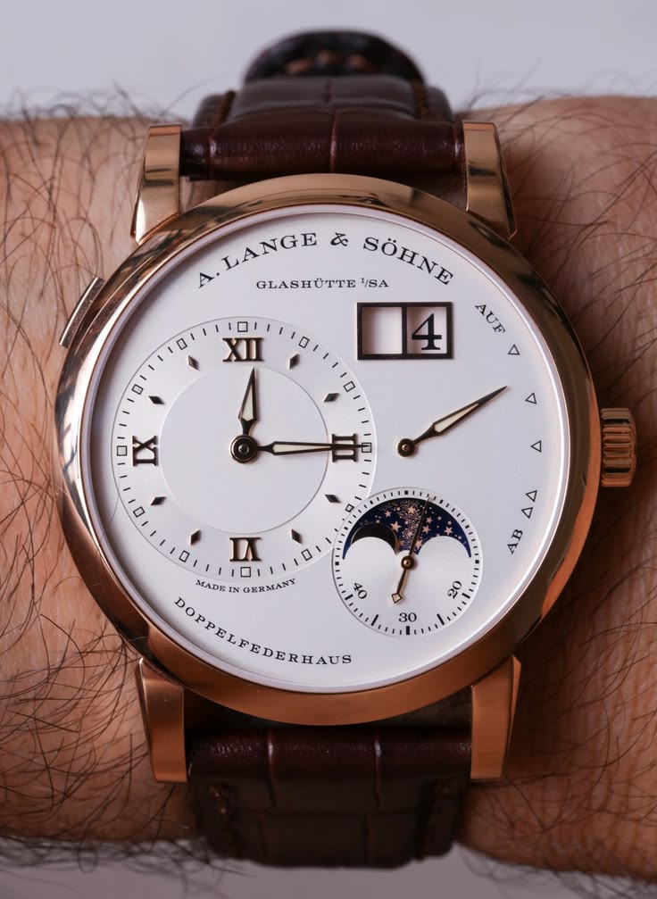 Wrist shot of an A. Lange & Söhne Lange 1 Moon Phase watch in 18k pink gold with a silver dial, outsize date, power reserve indicator, and brown alligator leather strap.