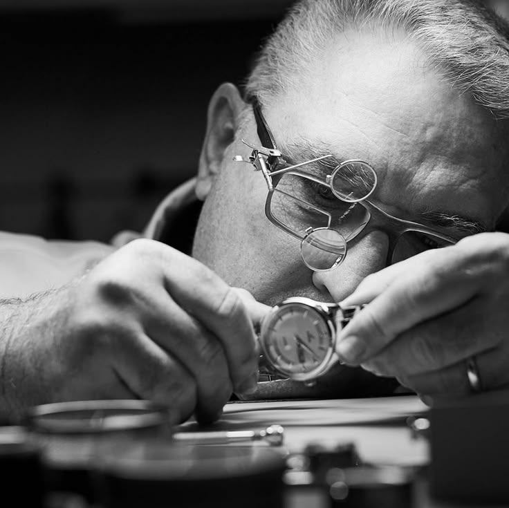 5 Watch Habits That Are Quietly Costing You a Fortune Close-up black and white shot of a skilled watchmaker wearing specialized magnifying loupe glasses while inspecting a precision wristwatch mechanism.