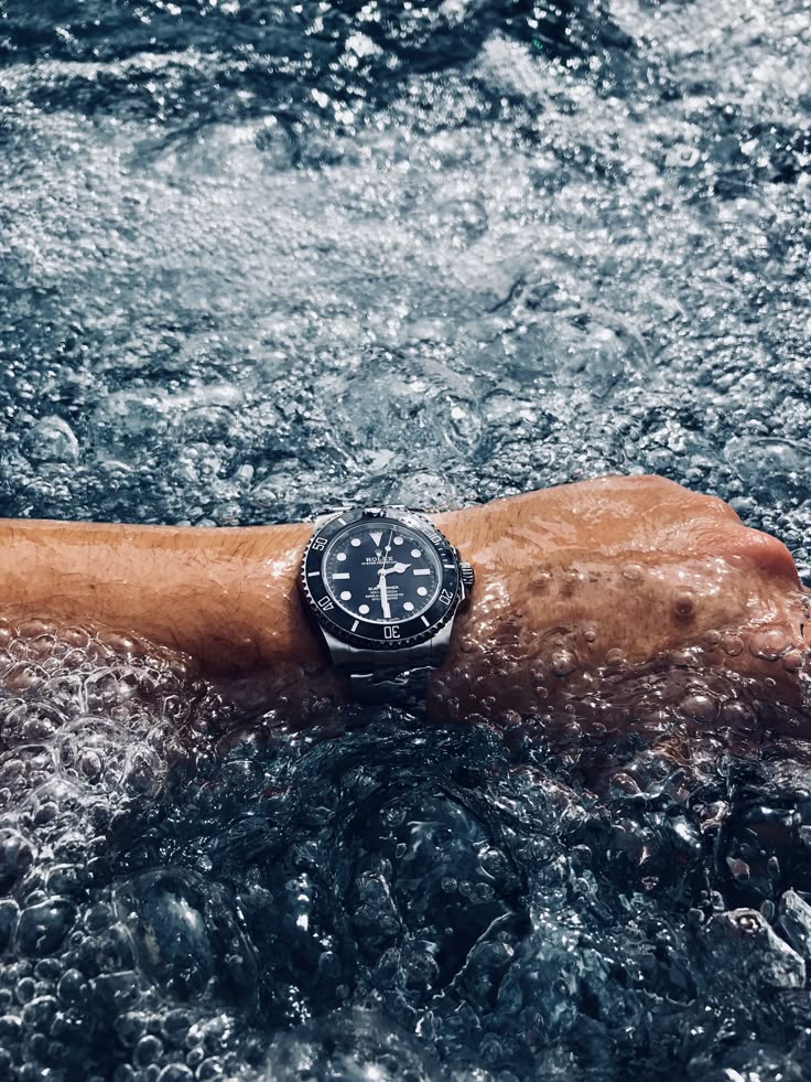 5 Watch Habits That Are Quietly Costing You a Fortune A close-up shot from above of a person's wrist wearing a Rolex Submariner diver's watch, which is submerged just below the surface in heavily bubbling, dynamic blue water.