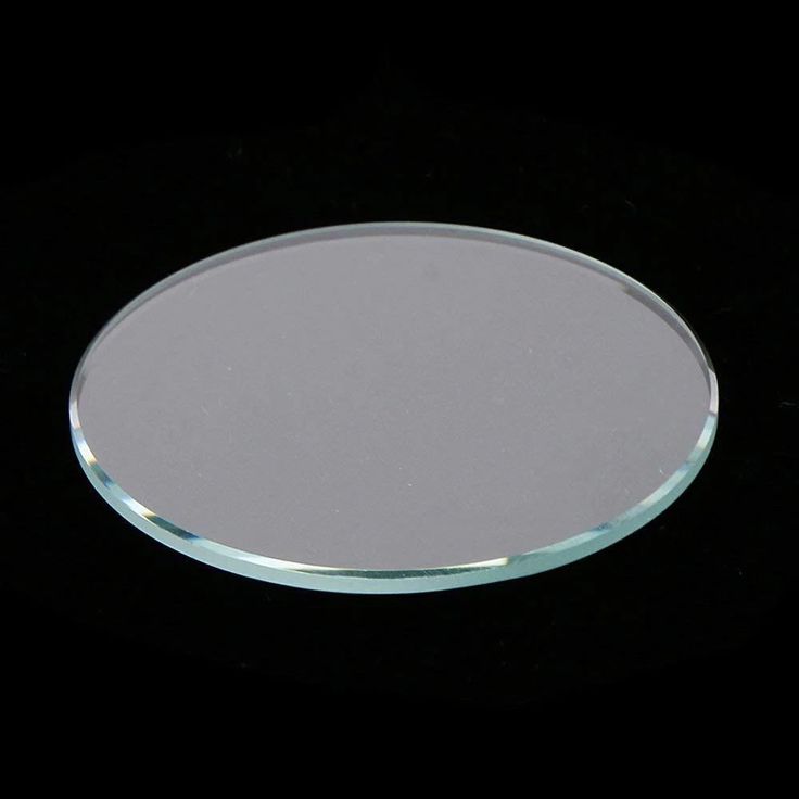 Clear, flat, circular watch crystal glass with beveled edges resting against a solid black background.